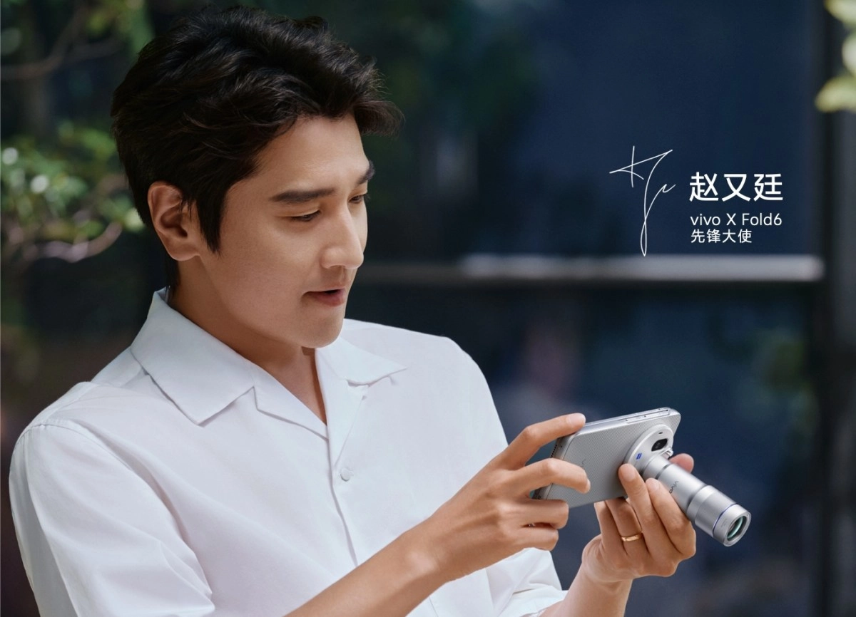 Man holds vivo X Fold6 with teleconverter lens.