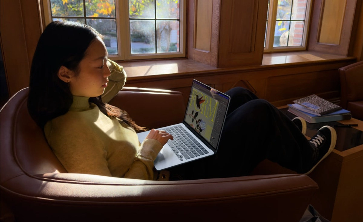 Woman using MacBook, studying by window.